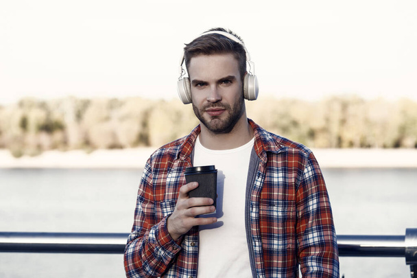 morning wake up. guy casual style drink take away coffee. time to relax. new digital technology. morning starts with fresh coffee. handsome young man in headphones. modern life. listen to music. - Foto, imagen