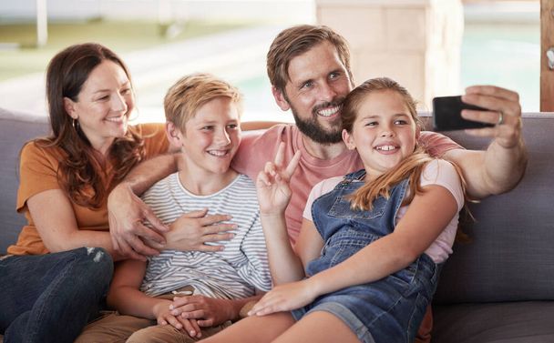 Teléfono, selfie y familia feliz en un sofá en la sala de estar relajarse juntos en su casa moderna. Felicidad, sonrisa y padres tomando una foto con sus hijos en un smartphone en su salón - Foto, imagen