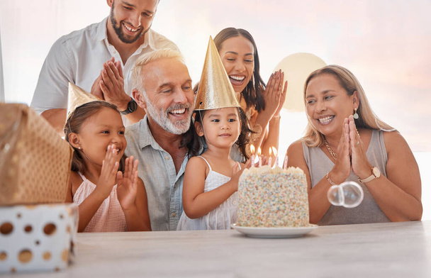 Family, birthday party and cake with celebration, clapping and singing with candle or gift on table in home. Girl, parents and grandparents with sister celebrate event in house with birthday cake. - Photo, image