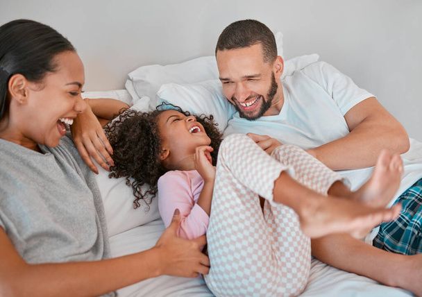 Family, parents and girl happy on bed, smile, laugh and bonding on weekend. Mom, dad or couple with kid happiness and love in pajamas, morning and being playful, care and fun together in bedroom - Photo, image