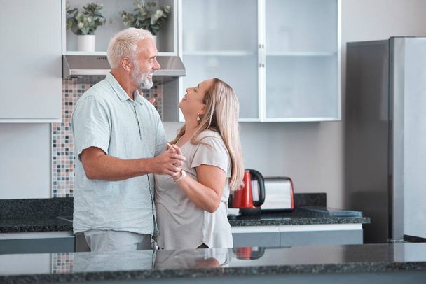 Love, dance and a senior couple in kitchen of home together enjoying weekend time and celebrate life with smile. Retirement, happiness and health, a happy man and woman dancing in house or apartment - Foto, imagen