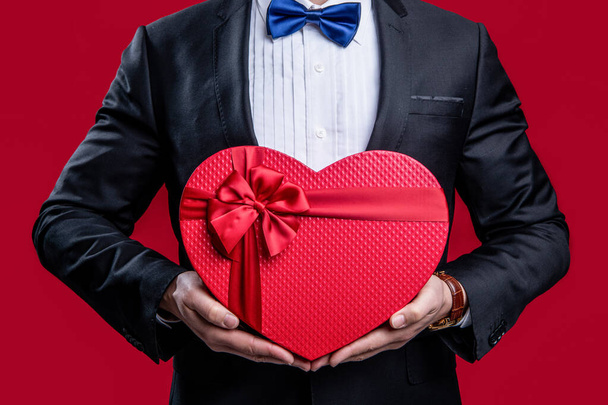 cropped man with proposal valentine gift. photo of tuxedo man hold proposal valentine gift. tuxedo man with proposal valentine gift isolated on red. tuxedo man hold proposal valentine gift in studio. - Foto, immagini