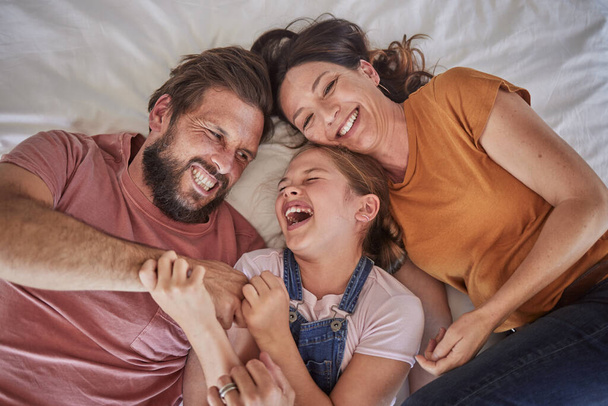 Family, bed and child with tickle, happy or comic play for quality time, bonding or home together. Above, parents and girl with happiness, laugh or crazy with love, mom and dad in happy family house. - Photo, image