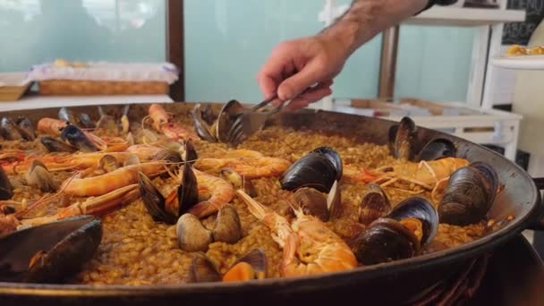 Fechar de um garçom servindo uma paella típica de frutos do mar espanhóis da paellera, a panela de paella, colocada em uma mesa para o almoço - Filmagem, Vídeo
