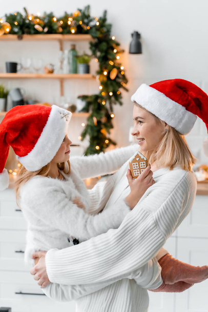 Linda joven madre e hija se divierten en la cocina disfrutando de la época de Navidad con galletas de Navidad preparaciones y luces - Foto, Imagen
