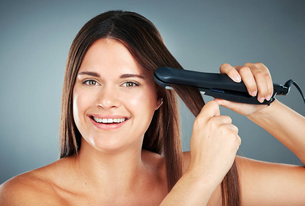 Beauty, hair care and flat iron with a model woman in studio on a gray background to straighten her hair. Wellness, growth and straight with an attractive young female using a hair straightener. - Фото, изображение