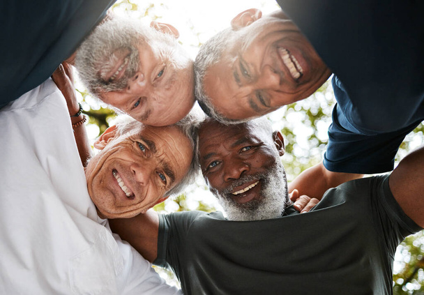 Vanhat miehet, huddle ja monimuotoisuus, ystävät ja tiimityöskentely ulkona solidaarisuuden, yhtenäisyyden tai unionin matalassa kulmassa. Iloisen ja vanhemman kuntoryhmän tuki, luottamus ja yhteistyö yhdessä harjoitustauolla - Valokuva, kuva