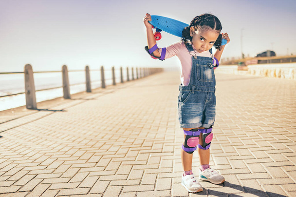 Portrait, skateboard and child in city, street or outdoors promenade ready for skating practice. Skateboarding sports, exercise and young girl preparing for training or fitness workout at seashore - Foto, imagen
