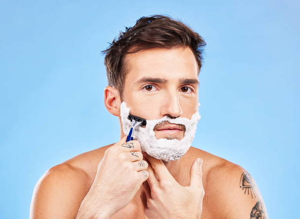 Stüdyoda sağlık ve bakım için mavi arka planda giyinen bir erkek modelle portre, tıraş ve tıraş makinesi. Yüzü, cildi ve tıraş olan yakışıklı genç bir erkek, yüz kıllarını aldırmak için banyoda.. - Fotoğraf, Görsel