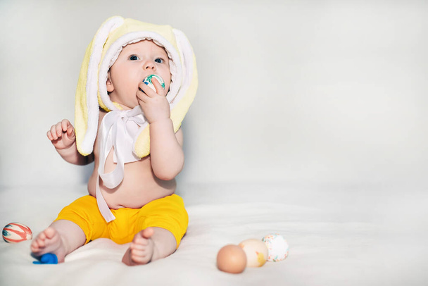 kleine mooie babysitter in geel verlichten konijn hoed. meisje viert Pasen en vond beschilderd decoratief ei speelgoed. liefde en religie concept. Kleur 2021 - Foto, afbeelding