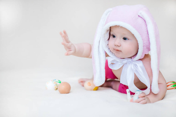 イースターのコンセプト。ウサギの帽子の女の子。子供はイースターエッグを持ってる。面白い幼児は嘘をつき、フレームに見える - 写真・画像