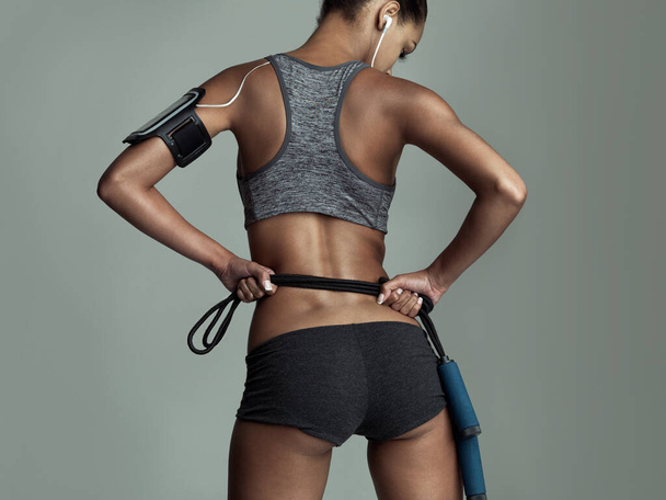 Fitness encarnado. Vista trasera del estudio de una joven mujer sosteniendo una cuerda sobre un fondo gris - Foto, imagen