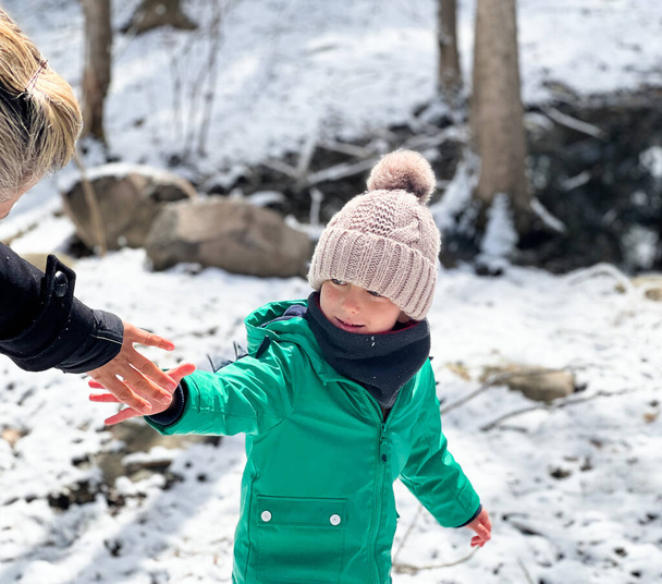 Boy wearing warm clothing holding mother's hand while standing on snow covered land in forest during vacation - Photo, Image