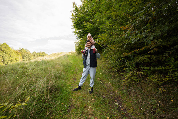 Папа с дочерью на плечах гуляет по лесу. - Фото, изображение