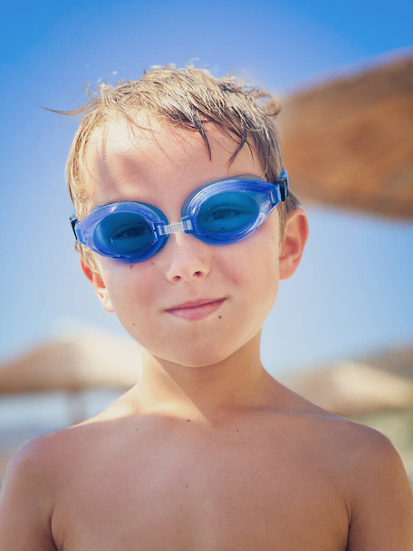 Gros plan portrait d'un garçon caucasien confiant portant des lunettes de natation bleues tout en profitant du week-end en plein air - Photo, image