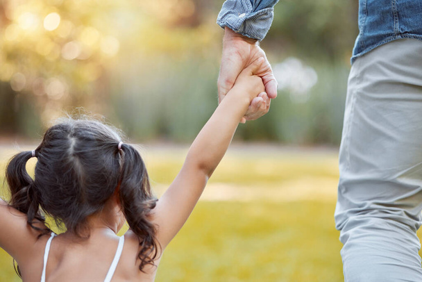 Holding hands, care and girl with father in a park with safety, support and security. Walk, trust and back of a child with dad in a backyard, field or nature in countryside for outdoor quality time. - Foto, Imagem