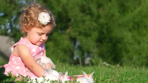 Malá holčička si hraje s bílým zajícem na zahradě sedícím na zelené trávě. Dítě si hraje s domácími mazlíčky v letní den. Zvíře je bílý zajíček. - Záběry, video