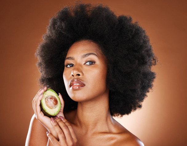 Avocado, black woman and skincare beauty for cosmetics, moisturizer or nutrition in brown studio background. Portrait of African American female holding fruit with diet for healthy facial treatment. - Фото, изображение