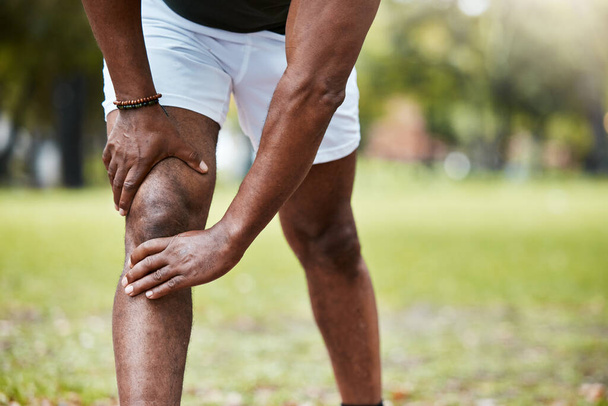 Αθλητισμός, φυσική κατάσταση και πόνο στο γόνατο του μαύρου άνδρα στο πάρκο μετά το τρέξιμο σε εξωτερικούς χώρους. Υγεία, ευεξία και ώριμος άνδρας δρομέας με τραυματισμό στο πόδι, μυϊκό πόνο ή φλεγμονή των αρθρώσεων μετά από προπόνηση ή προπόνηση - Φωτογραφία, εικόνα