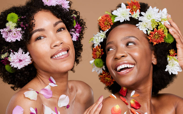 Women, beauty and flowers in studio for wellness, cosmetic and grooming on brown background. Flower, crown and black woman friends relax, hygiene and pamper, nature product and zen plant aesthetic. - Foto, Imagem