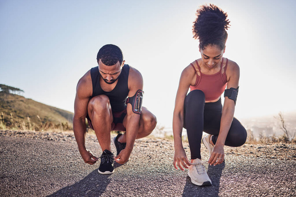 Fitness couple, running shoes and exercise on a road outdoor for cardio workout and training together for health and wellness. Black woman and man tying shoelace or sneakers for a agile run. - Zdjęcie, obraz