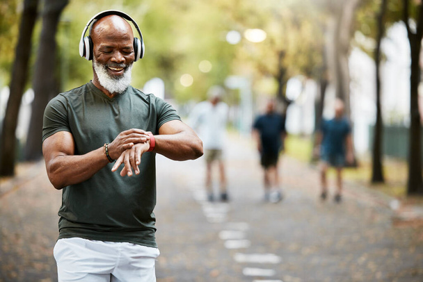 Music, time and running with a mature black man looking at his watch while out for a fitness run in the park. Workout, wellness and training with a senior male athlete or runner tracking his health. - Фото, зображення