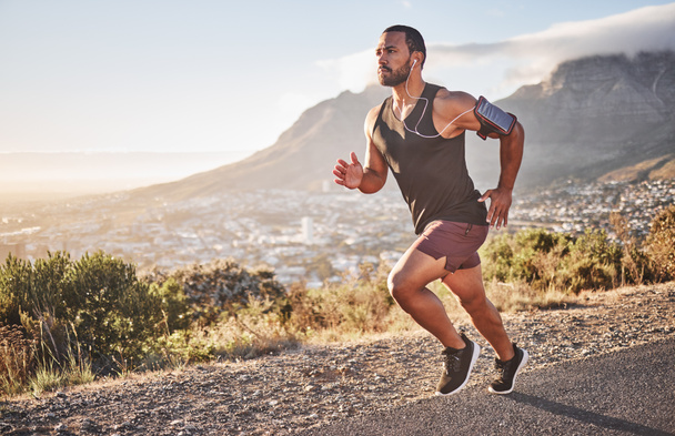 Fitness, sports and man running on mountain with city background doing marathon training. Speed, endurance and athlete with headphones listening to music doing exercise, workout and sport performance. - Photo, Image