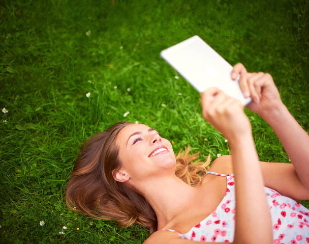 Encontrar algunas cosas interesantes en línea. una mujer joven que usa su tableta digital mientras está acostada en la hierba - Foto, Imagen