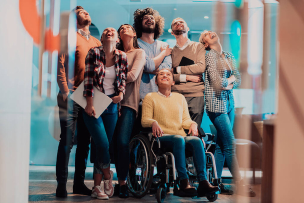 Businesswoman in a wheelchair on break in a modern office with her team in the background. High quality photo - Foto, Bild