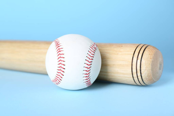 Wooden baseball bat and ball on light blue background, closeup. Sports equipment - Photo, image