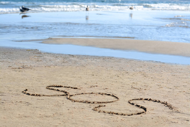 SOS message written on sand near sea - Foto, Bild
