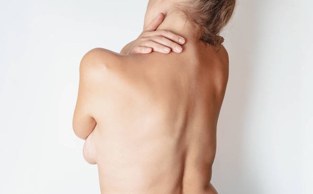 Mujer desnuda con dolor de cuello y espalda sobre fondo blanco. Vista trasera
. - Foto, imagen