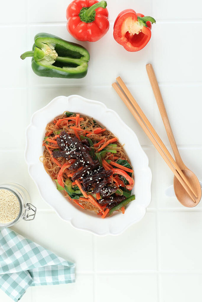 Japchae Wjite Bowlissa Valkoisella pöydällä. Korealainen keittiö lasi Chapchae nuudelit lautasen vihanneksia ja naudanlihaa Bulgogi. Aasian Perinteinen Aito Ruoka. Ylhäältä - Valokuva, kuva