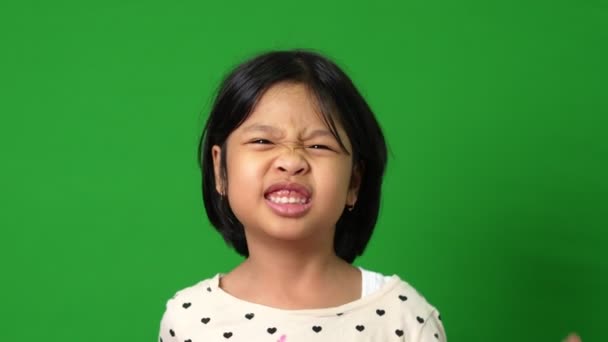 Portret van een vrolijk en grappig Aziatisch meisje op een groene achtergrond, een kind dat naar de camera kijkt. kleuter dromen vullen met energie gevoel gezond en goed concept - Video