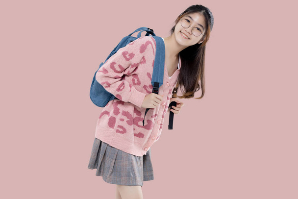 Ευτυχισμένη Ασιατική εθνικότητα έφηβος κορίτσι κρατήσει σακίδιο απομονωμένο σε παστέλ ροζ φόντο. Εκπαίδευση στο γυμνάσιο έννοια κολέγιο. - Φωτογραφία, εικόνα