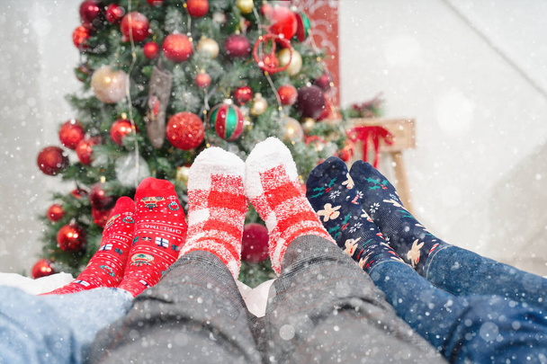 menschliche Füße auf dem Bett in Weihnachtssocken auf dem Hintergrund des Weihnachtsbaums. Weihnachtssocken aus nächster Nähe. Weihnachten gemütlichen Hintergrund - Foto, Bild