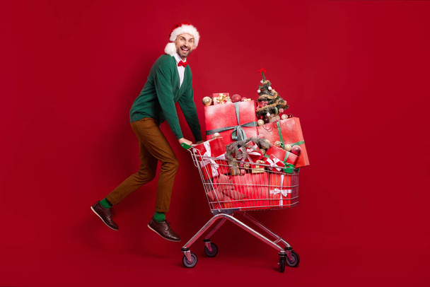 Full length portrait of excited energetic guy jumping push market trolley pile stack decor giftbox isolated on red color background. - Fotoğraf, Görsel