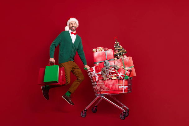 Full length photo of funky jumping air with shopping cart with giftboxes winter season sale hold bags excited isolated on red color background. - Fotó, kép