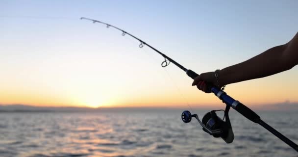 Handen van de visser houdt draaiende staaf met haspel op de achtergrond van de zee. Hobby visserij en toerist - Video