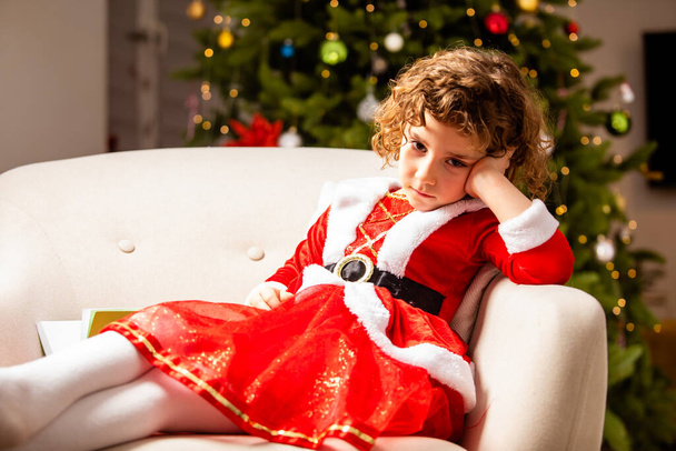 Adorable girl in Christmas dress near the classic decorated christmas tree with lights - Zdjęcie, obraz