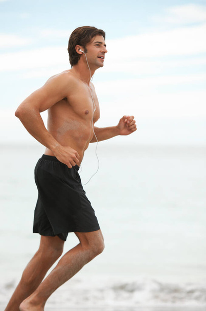 Tunes to workout to. a handsome young man going for a run on the beach while listening to music - Fotografie, Obrázek