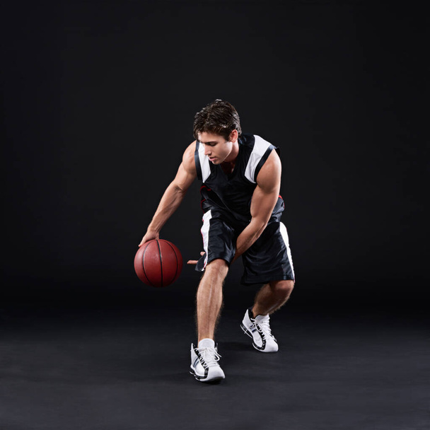 Hij speelt om te winnen. Volledige shot van een mannelijke basketbalspeler in actie tegen een zwarte achtergrond - Foto, afbeelding