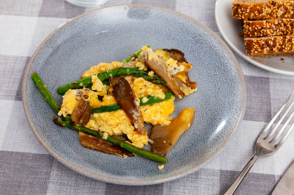 Portion of scrambled eggs with asparagus and mushrooms served on table. - Fotó, kép