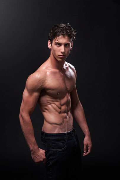 I like my muscles lean and mean. Studio shot of a handsome bare-chested young athlete standing against a black background - Foto, Bild