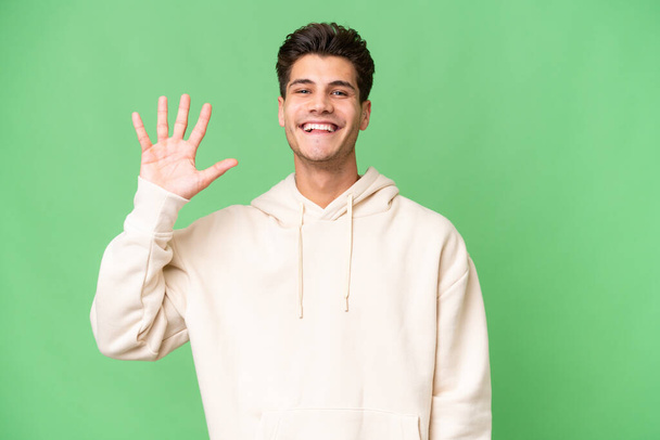 Young caucasian handsome man over isolated background saluting with hand with happy expression - Фото, зображення