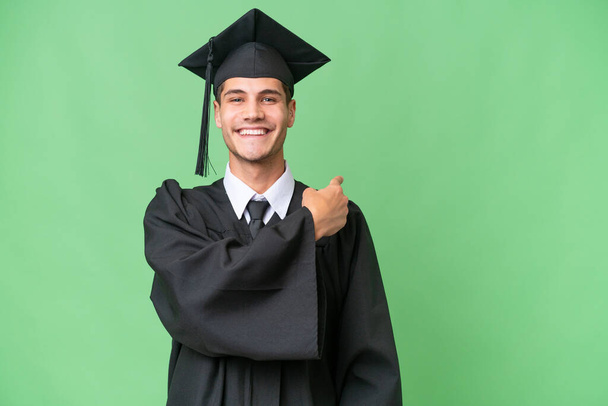 Молодий випускник університету кавказький чоловік над ізольованим фоном, що вказує назад
 - Фото, зображення