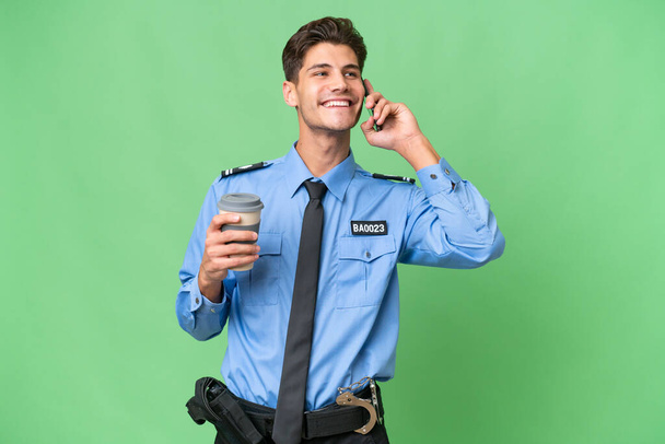 Jeune policier sur fond isolé tenant un café à emporter et un mobile - Photo, image