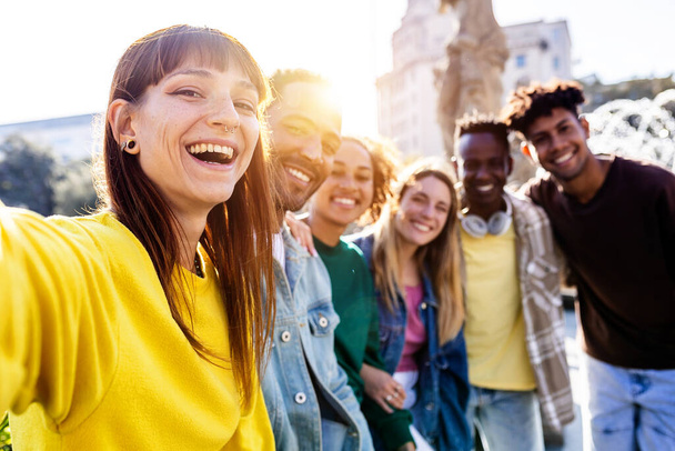 Usmívající se tisícileté kamarádky se baví focením selfie portrétu venku. Různí teenageři hledící na kameru stojí ve frontě na fotografickou skupinu. Multiraciální koncept přátelství - Fotografie, Obrázek
