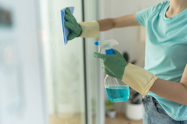 Женская рука в зеленых перчатках, чистка дверей с голубой тряпкой и моющим средством. - Фото, изображение