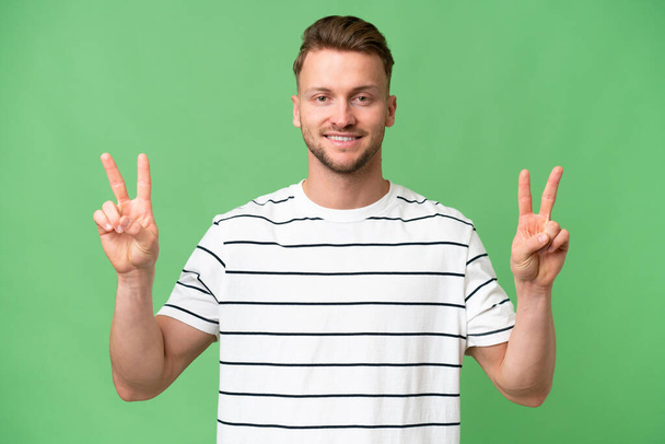 Young blonde caucasian man over isolated background showing victory sign with both hands - Photo, Image